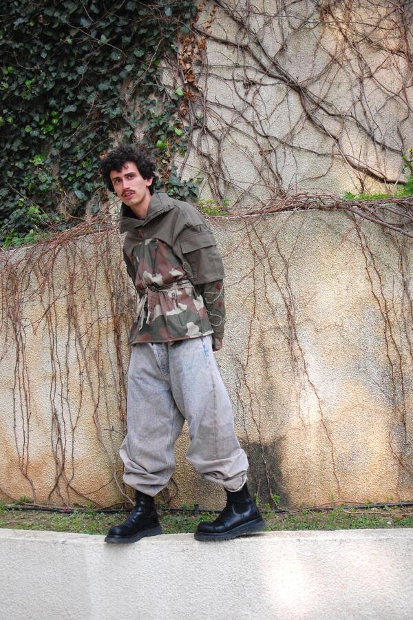 The full look against a vine-covered wall, worn with wide grey trousers and boots.